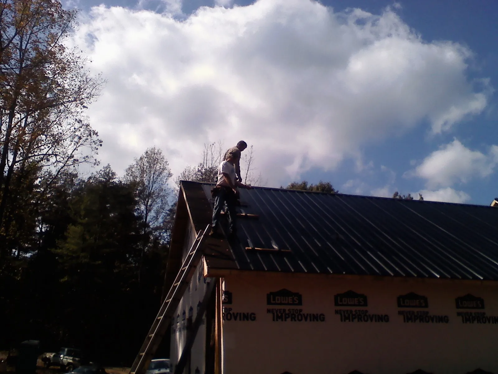 Roofer fastening dark metal panels high against a cloudy sky, from a Roof Inspection job in Front Royal