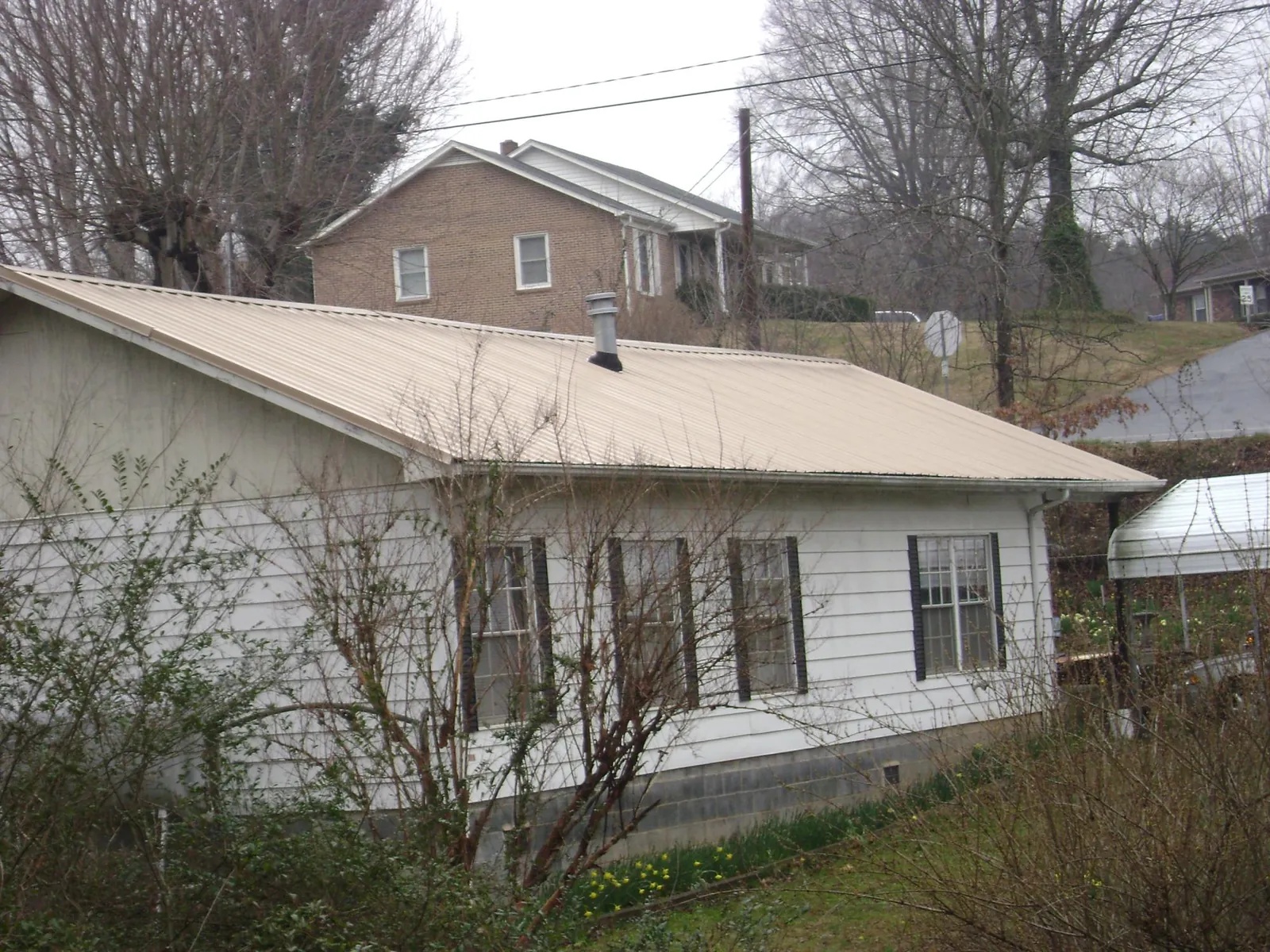 Tan metal roof on a white sided house set into a hillside — Commercial Roofing by Roofing Brothers in Front Royal